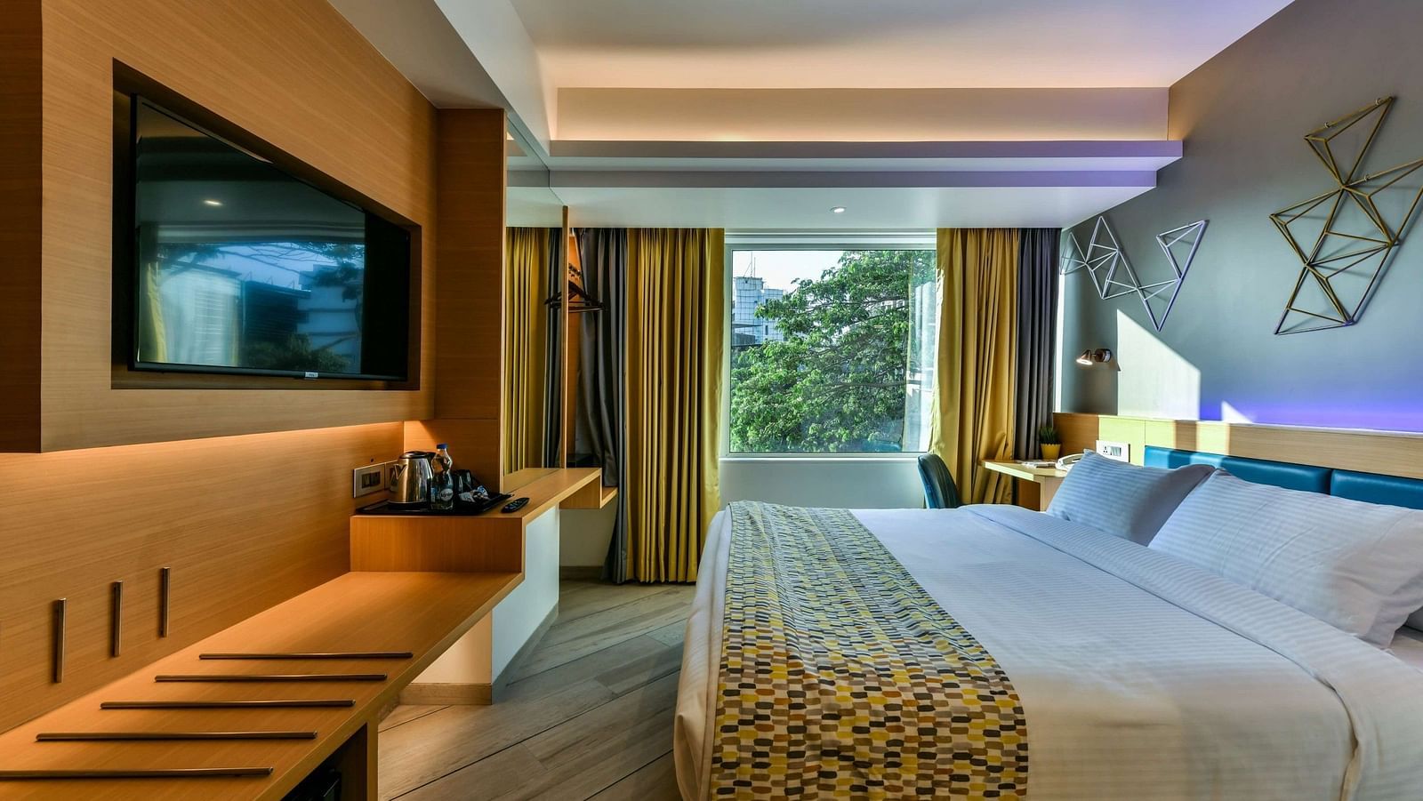 A spacious room featuring a large bed and a window with curtains pulled to the side, offering a view of trees, at Indie Stays, BKC Kalina.