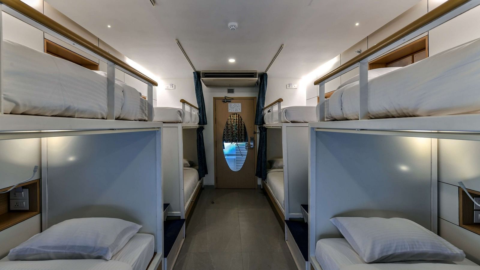 A pair of bunk beds placed on either side of the room, with a wooden door featuring an oval-shaped mirror at the far end, at Indie Stays, BKC Kalina.