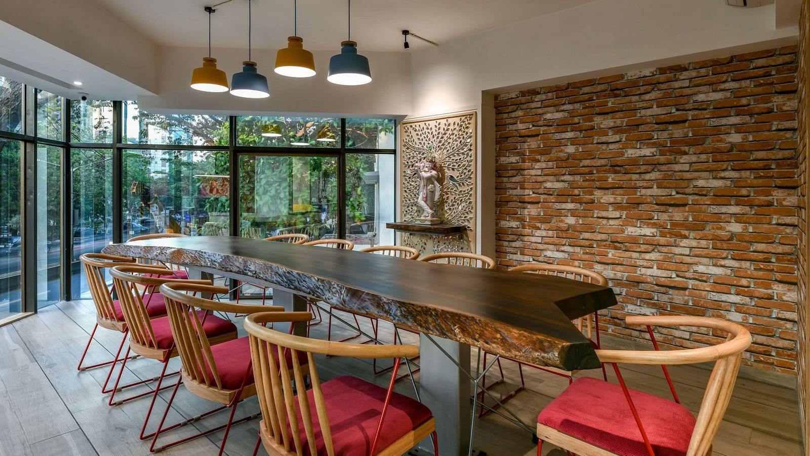 A large wooden table with chairs arranged around it, illuminated by hanging lights from the ceiling, at Indie Stays, BKC Kalina.