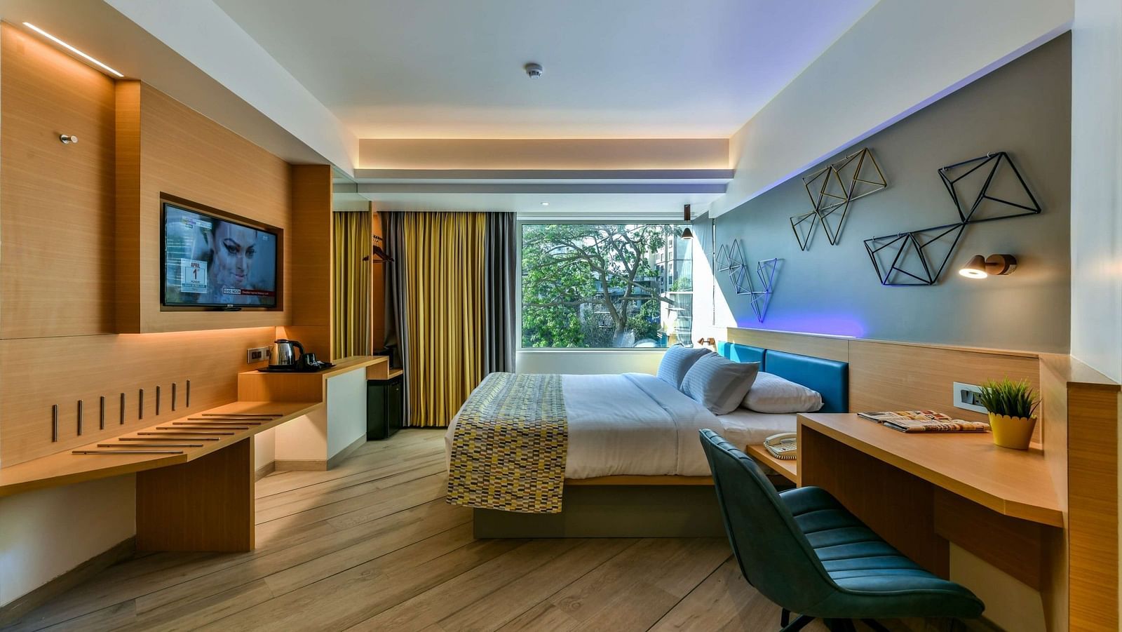 A spacious room with a large bed, a work desk and chair next to it, and a window offering a tree view, at Indie Stays, BKC Kalina.