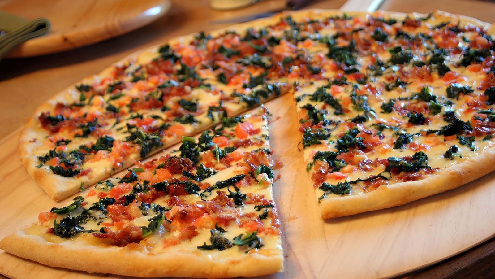 Pizza on a wooden plate with a single triangular slice cut out and placed slightly aside at Indie Stays, Jaipur.