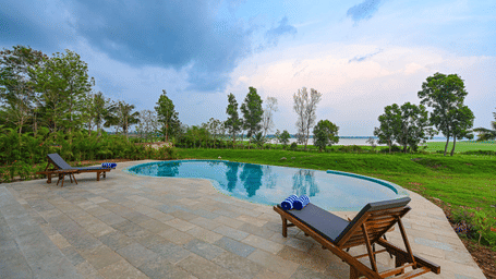 Infinity pool at Fireflies Resort Kabini with lounge chairs, lush greenery, and scenic views under a partly cloudy sky