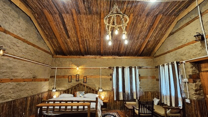 Full view of the Hamta Peak Cottage with brightly-lit interiors featuring wooden ceiling along with a double bed and a common seating area beside it at Amara Upepo - The Sky Village, Manali.