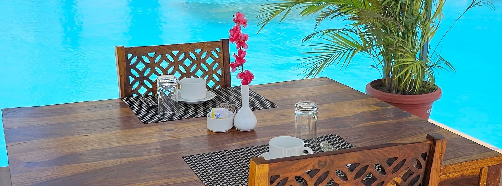 Shot of a wooden table and two chairs set beside a bright blue swimming pool - Bamboo Saa Mulberry Resort, Pushkar