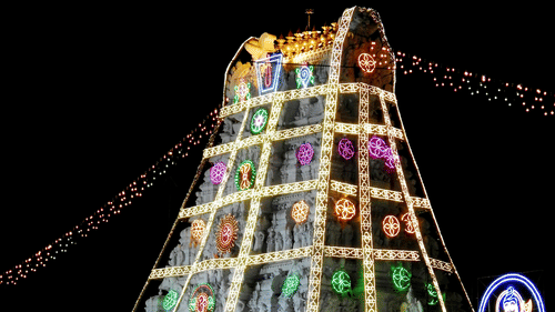 The Venkateswara Temple in Tirumala, India, is illuminated at night, showcasing its pyramid-shaped structure adorned with colourful lights and intricate carvings.