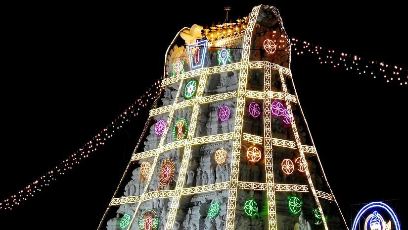 The Venkateswara Temple in Tirumala, India, is illuminated at night, showcasing its pyramid-shaped structure adorned with colourful lights and intricate carvings.