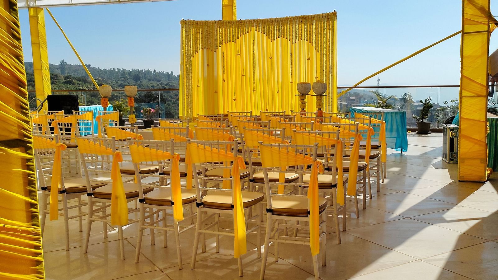 A courtyard where several chairs with yellow fabrics are set up near a stage which is also decorated by yellow fabrics and  flowers  where people are going to gather for pre wedding functions at The Grand Legacy Resort & Spa