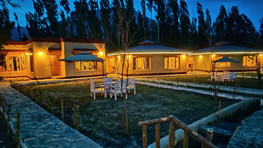 Night view of White Sand Resort, Ladakh showing illuminated buildings and surrounding trees.