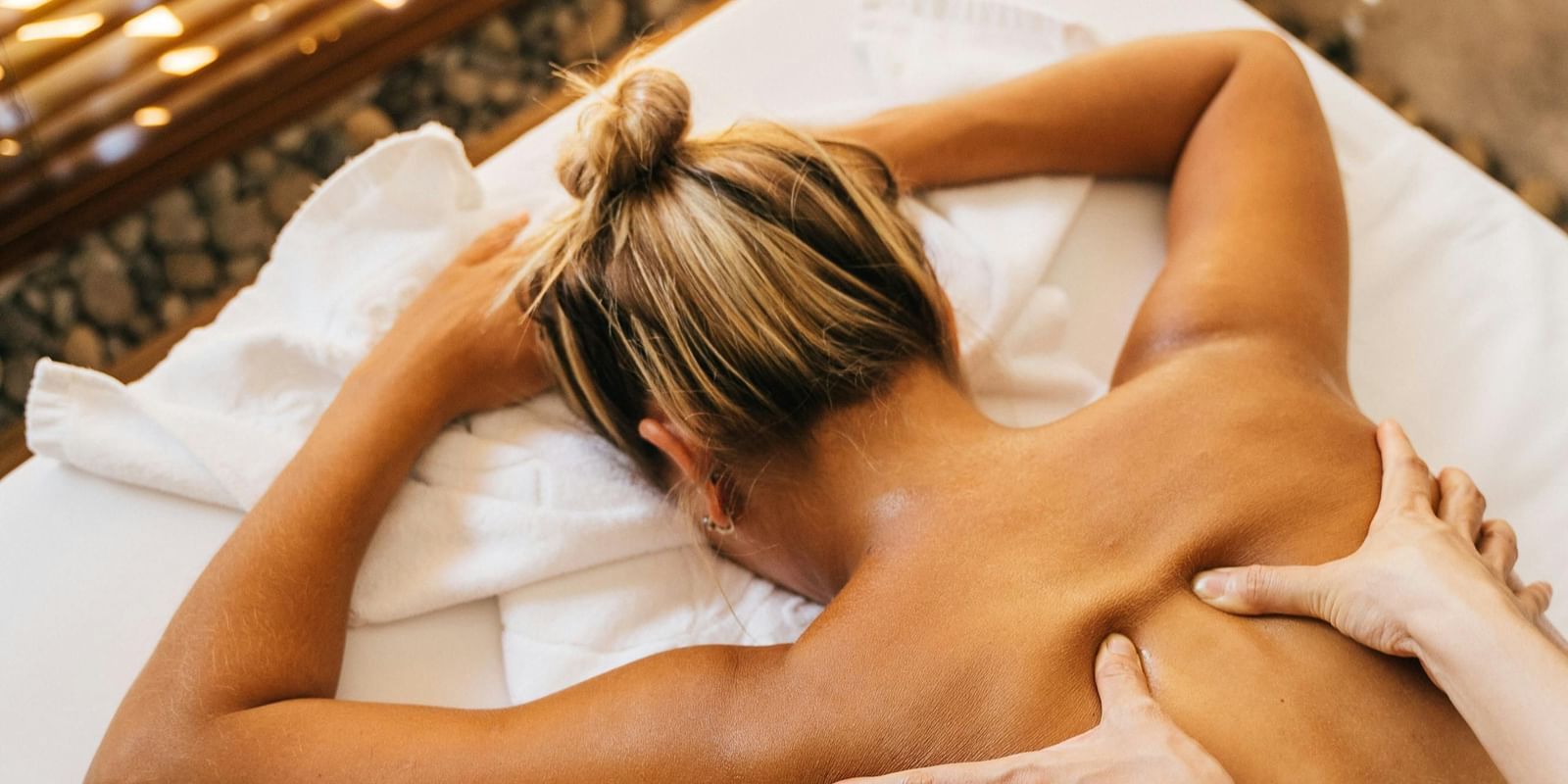 A top-down shot of a person receiving a back massage on a massage table, with the masseuse's hands applying pressure to their back.