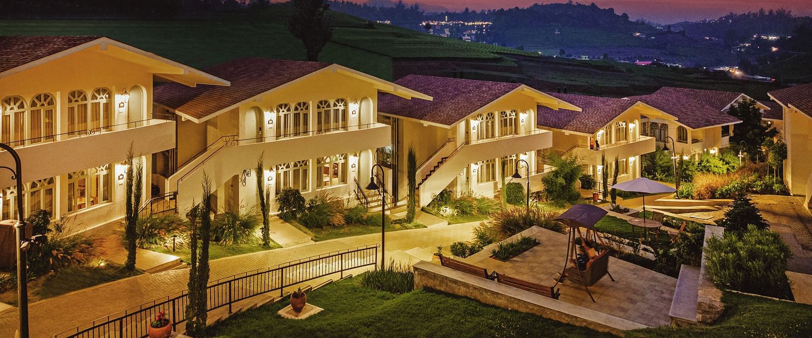 Aerial view of Mango Hill Shola, Ooty, with tiled-roof buildings arranged around a paved pathway and bordered by trees.