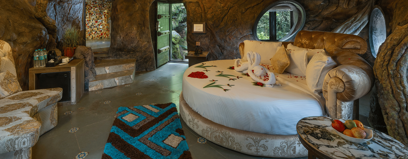 The bedroom of the Cave Room at Parakkat Nature Hotel and Resorts, Munnar, featuring a large circular bed, decorative light fixtures, and walls designed to resemble natural rock formations.