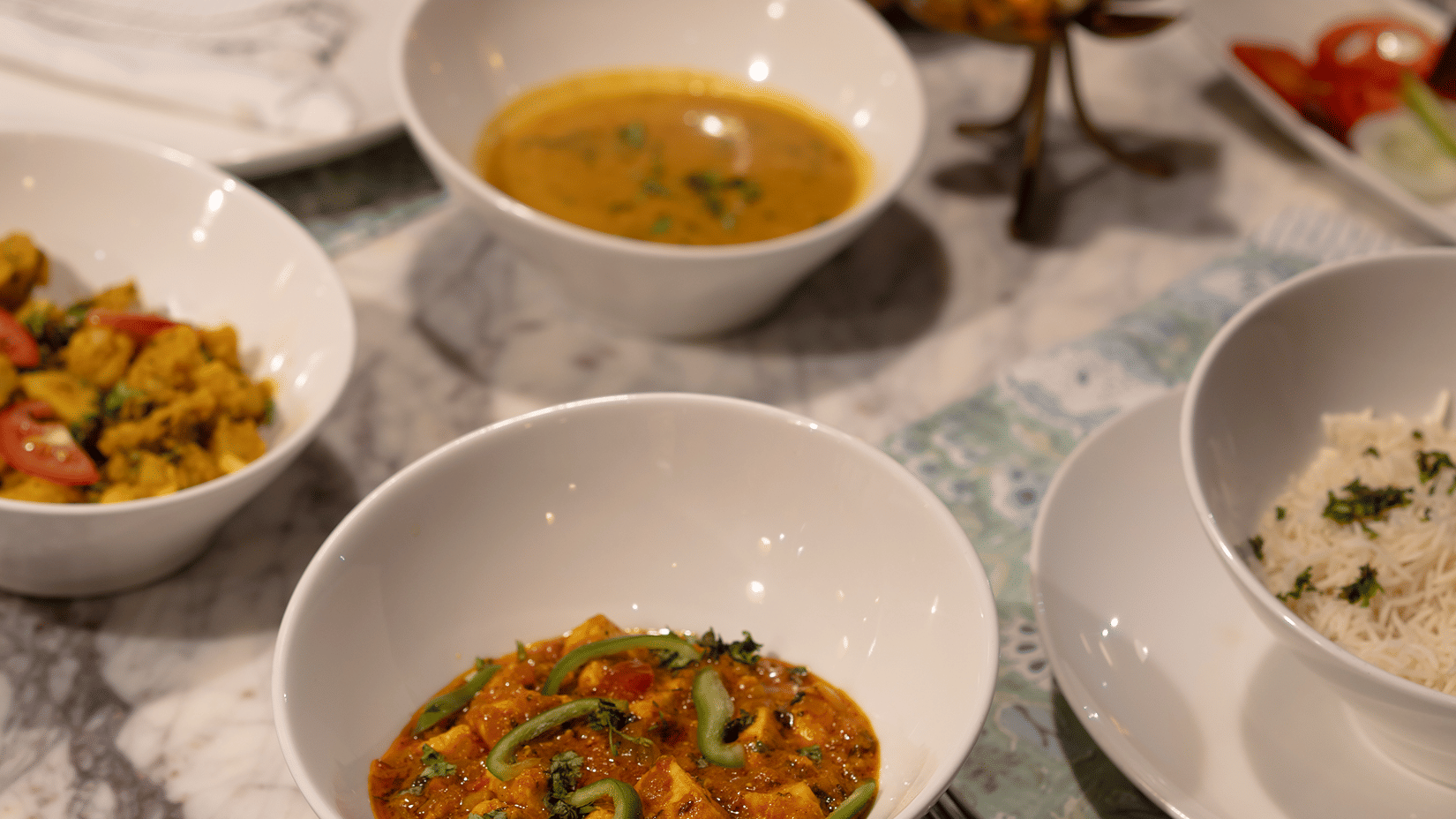 Table setting with delicious bowls of fresh curry, soup, and rice under warm ambient candle lighting.