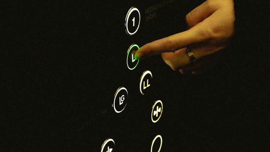 Hand pressing a lit elevator button on a dark control panel.