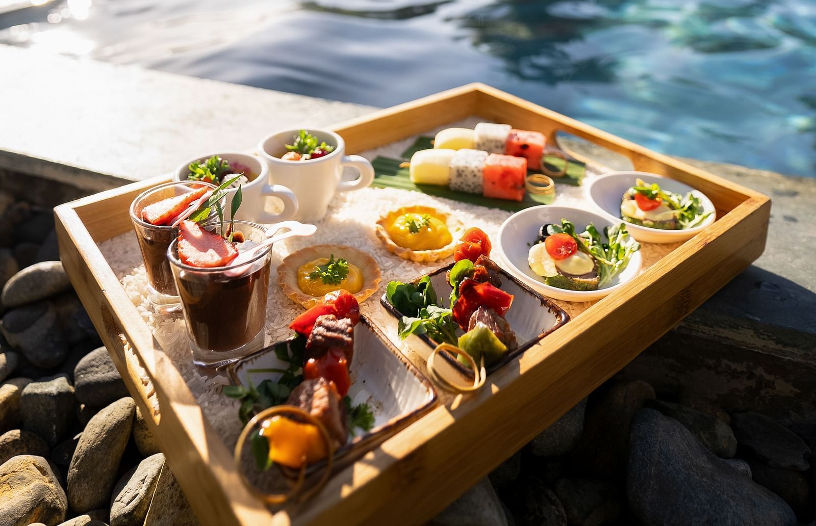 A wooden tray filled with food sits poolside, ready for a delicious meal with a scenic view.