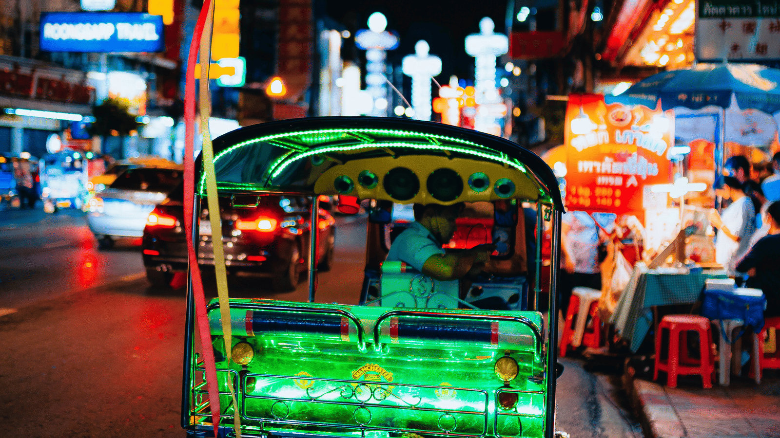 A parked tuk tuk with neon lights at the back and the driver sitting inside.