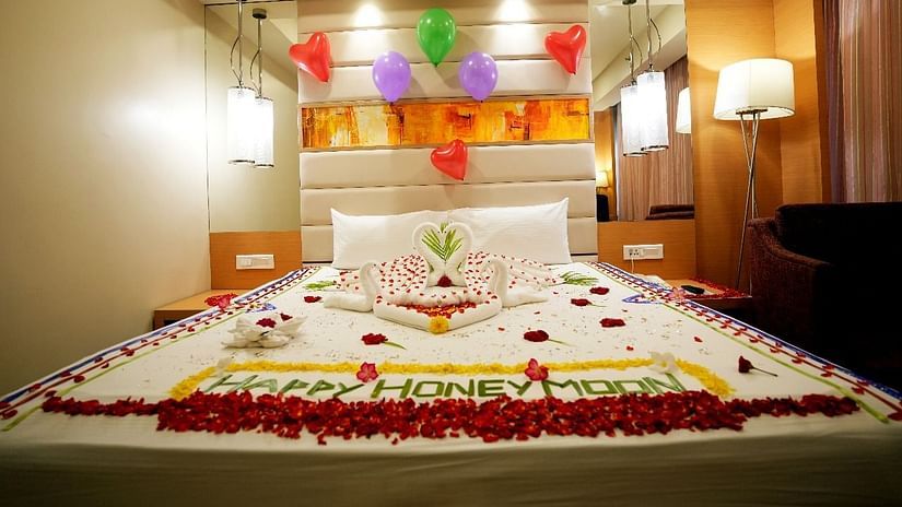 A luxurious hotel room with a beautifully decorated bed adorned with flowers and elegant lighting for Honeymoon