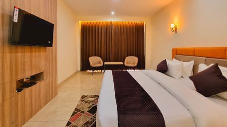 Side view of a room with bed, television mounted on the wall and seating area in the corner at Pines and Peaks, Dalhousie 