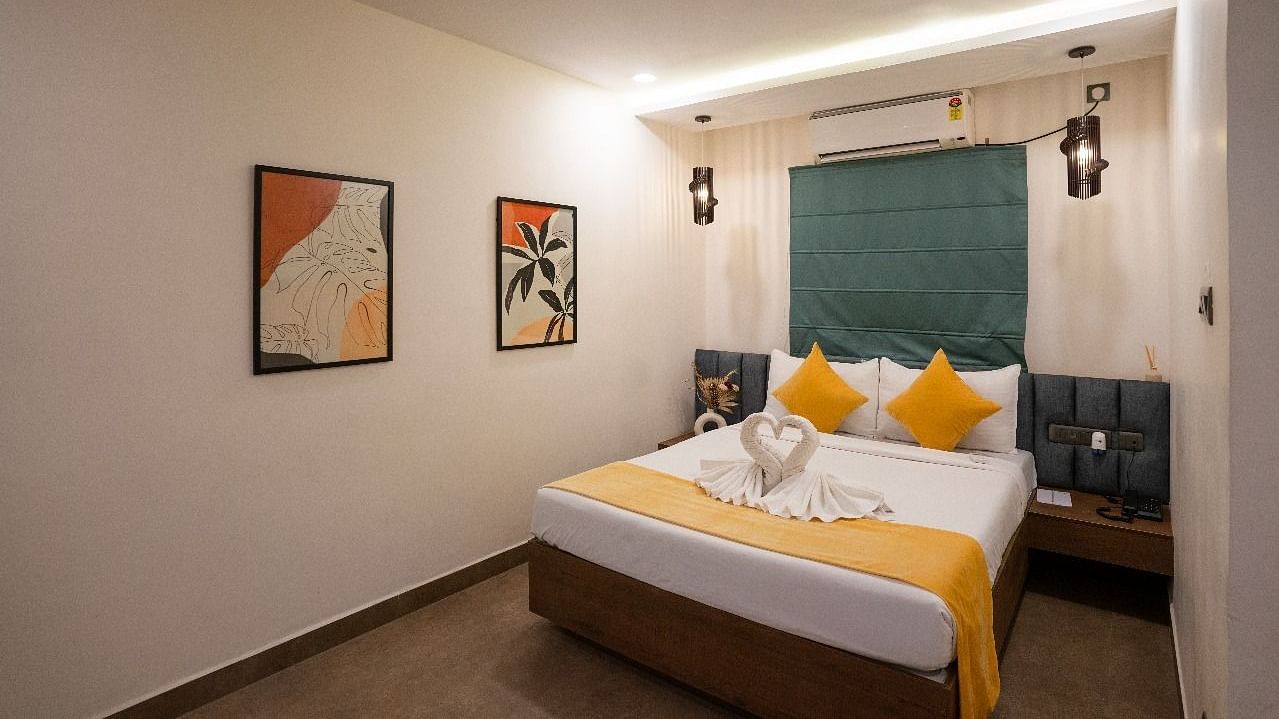 A side view of the room showcasing the bed, warm lighting, wall decor, and a large window offering natural light at Kyzen Smart Stays.