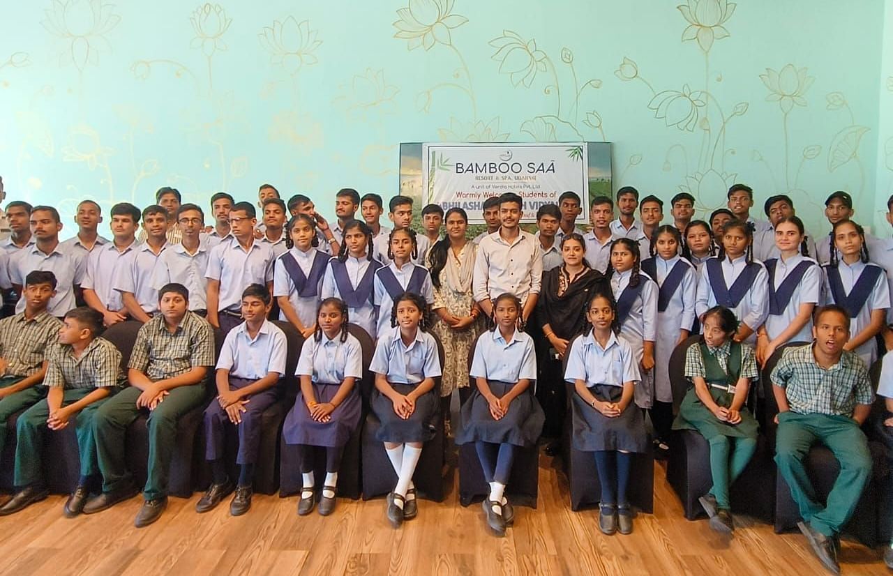 A large group of students in uniforms and adults posing for a photo in a brightly lit room - Bamboo Saa