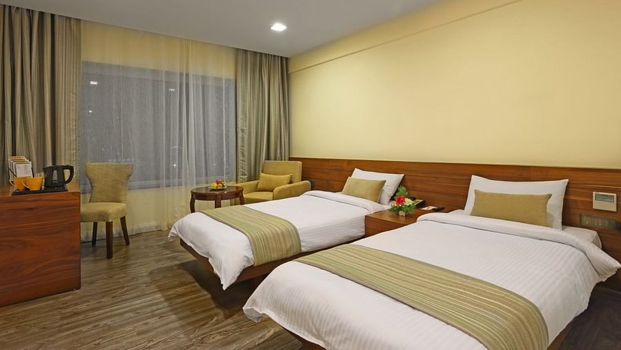 Twin bed with cosy comforters, on a well lit room, with a coffee table table and a chair