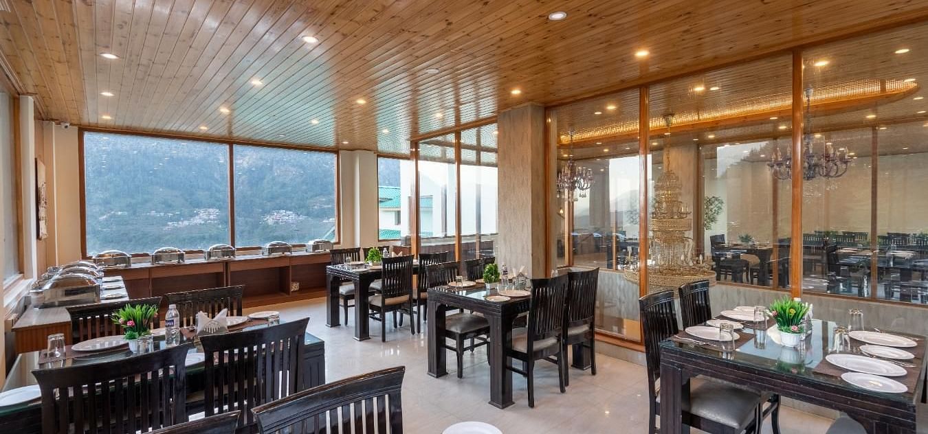 The image showcases a contemporary restaurant with large windows framing stunning mountain views  | DLS Serenity Resort and Spa