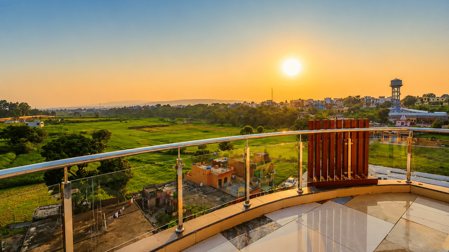 Private balcony seating with railing overlooking open fields at sunrise at Eastlynn Resort, Rishikesh.