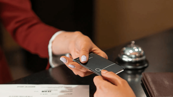 Close-up of a guest's hand receiving a key card from a receptionist at a front desk.