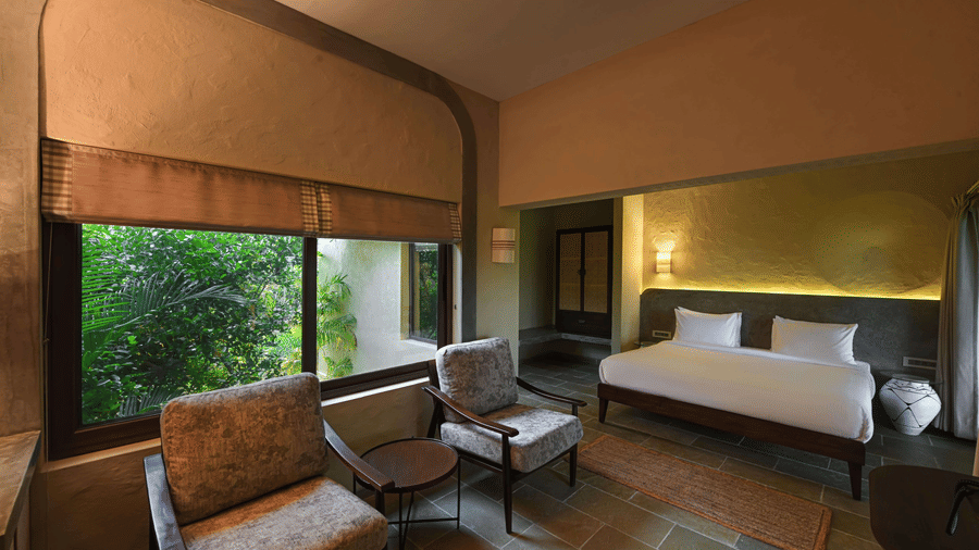 Luxury suite at Fireflies Resort Kabini with king bed, leather seating area, and floor-to-ceiling windows overlooking greenery.