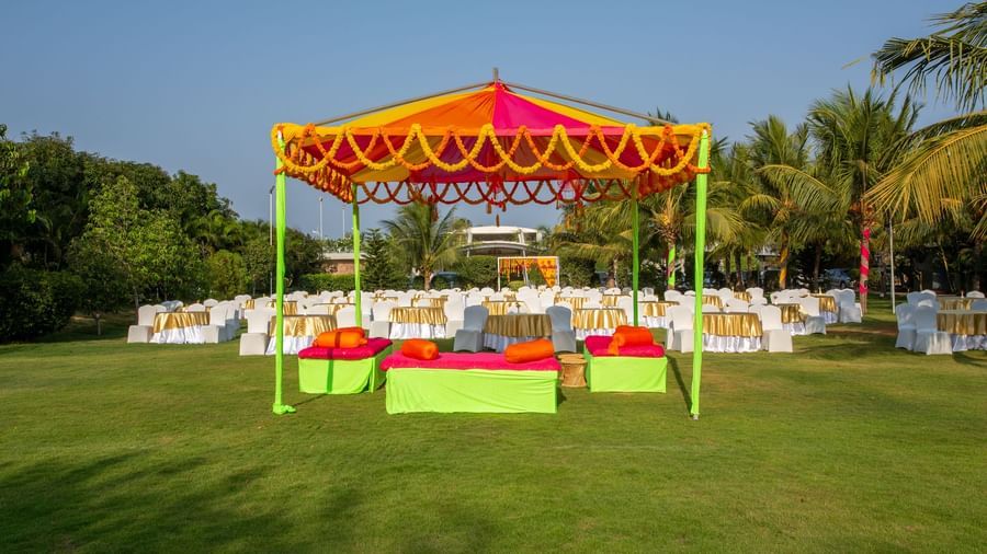 A colorful outdoor event setup featuring an orange and yellow tent, vibrant green and pink seating, and round tables on a manicured lawn | Grande Pavillion | Grand Bay Resort and Spa