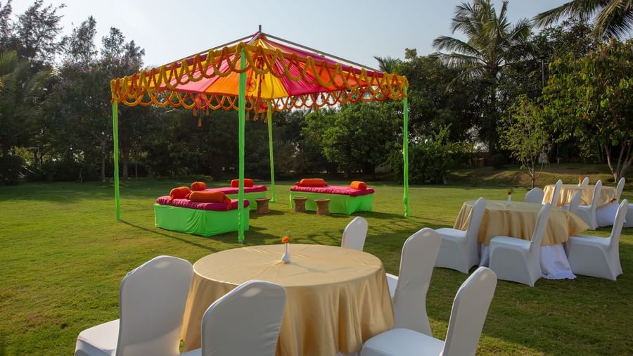 An outdoor event setup with a yellow and orange tent, green and red seating, and round tables on a vibrant green lawn | Citrus Garden | Grand Bay Resort and Spa