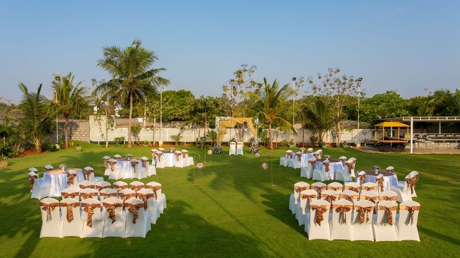 An outdoor event setup on a green lawn with neatly arranged tables and chairs, some covered in sashes, under a clear sky | Grande Pavillion | Grand Bay Resort and Spa