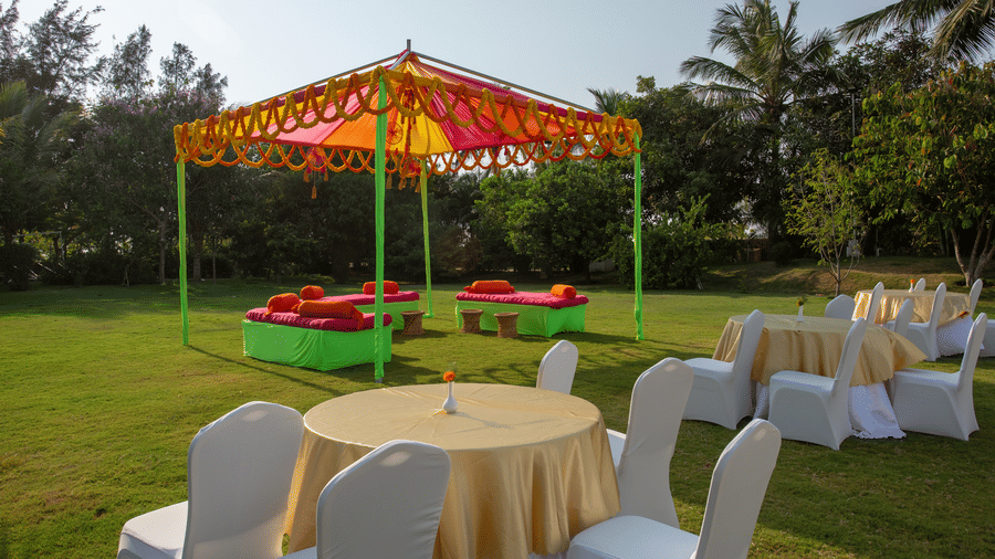 An outdoor yellow and orange tent hosting green and red seating, and round tables on a vibrant green lawn - Grande Bay Resort & Spa, Mamallapuram