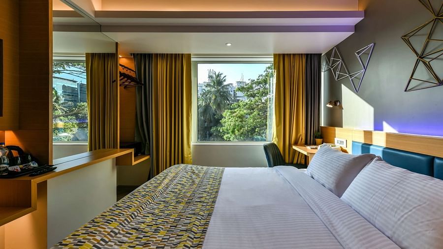 A spacious room featuring a large bed and a window with curtains pulled to the side, offering a view of trees, at Indie Stays, BKC Kalina.