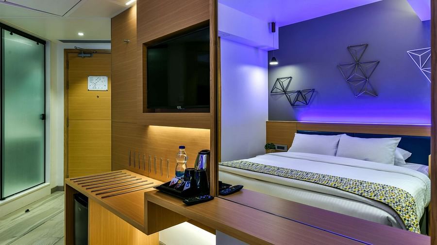 A two-image collage showcasing a spacious bed in one frame and a wall-mounted TV alongside tinted glass sliding doors leading to the washroom in the other, at Indie Stays, BKC Kalina.