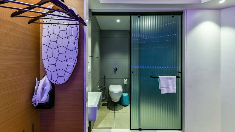 A wooden wardrobe with hangers, providing a view of the washroom entrance through a tinted glass door, at Indie Stays, BKC Kalina.