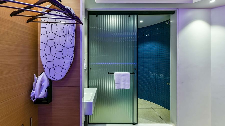 A wooden wardrobe with hangers, offering a view of the washroom entrance through a tinted glass door, at Indie Stays, BKC Kalina.