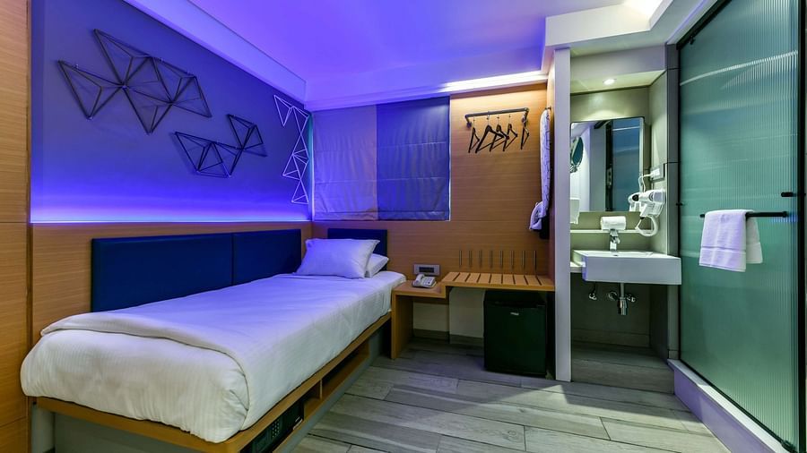A spacious room with a single bed, a wooden wardrobe, and cool lighting at Indie Stays, BKC Kalina.