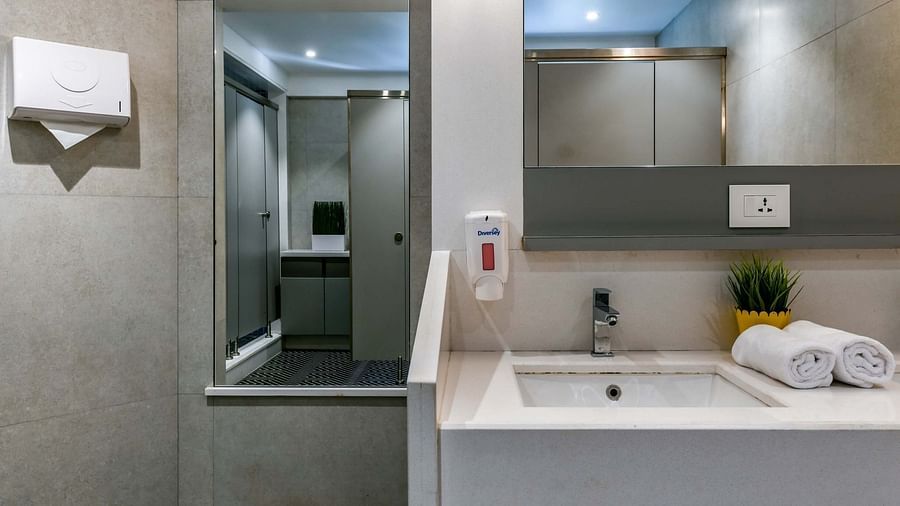 A washroom with a portrait and mirror, a landscape mirror above the washbasin, wall-mounted tissue box, and essentials like hand wash and rolled towels on the counter at Indie Stays, BKC Kalina.