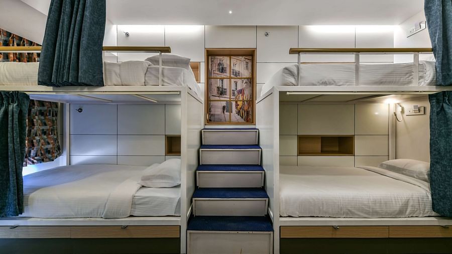 A pair of bunk beds with curtains pulled to the side, a staircase placed in the middle, and bright lighting at Indie Stays, BKC Kalina.
