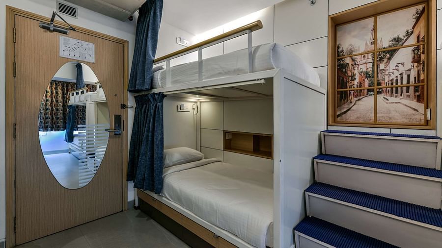 Bunk beds with curtains pulled to the side, accompanied by stairs and a wooden door with an oval-shaped mirror at Indie Stays, BKC Kalina.