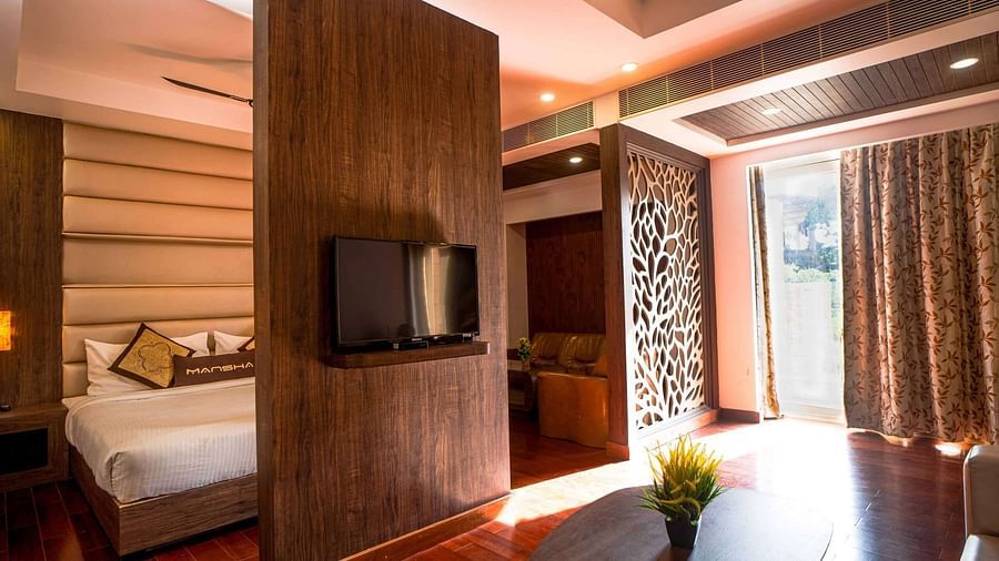 A hotel room interior with a wooden partition separating the sleeping area from a living, featuring warm lighting at Mansha Hotel Regency.