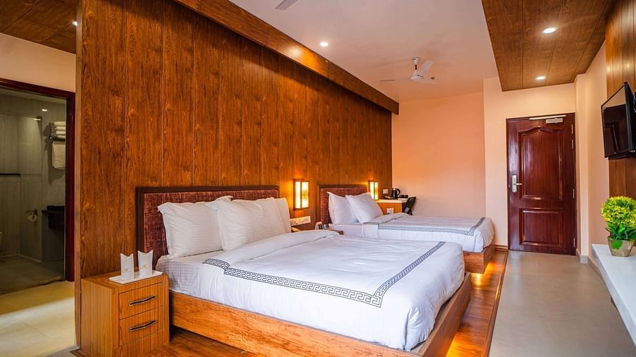 A comfortable hotel room at Mansha Palace features two beds, wooden accents, and a glimpse into the bathroom.