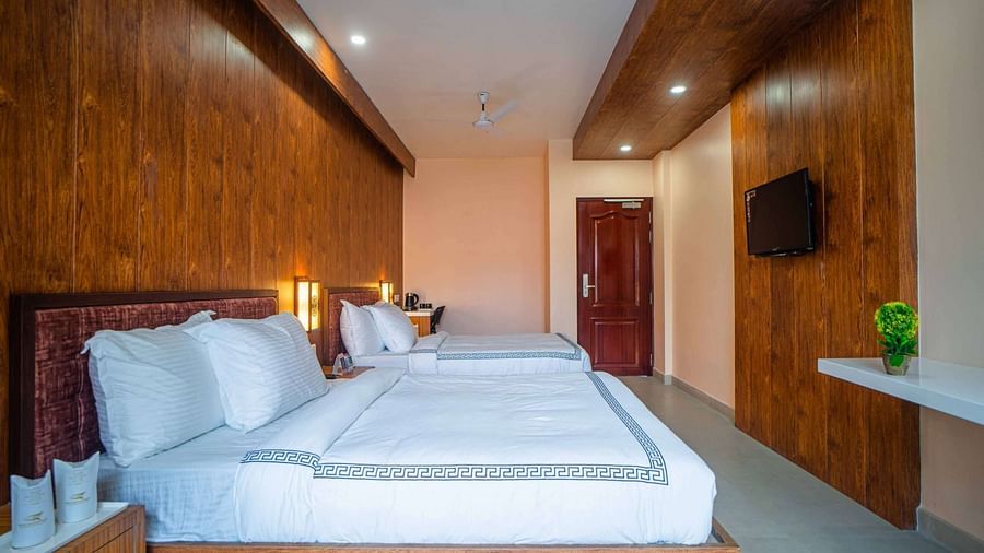 A comfortable hotel room at Mansha Palace features two beds, wooden accents, and a glimpse into the bathroom.