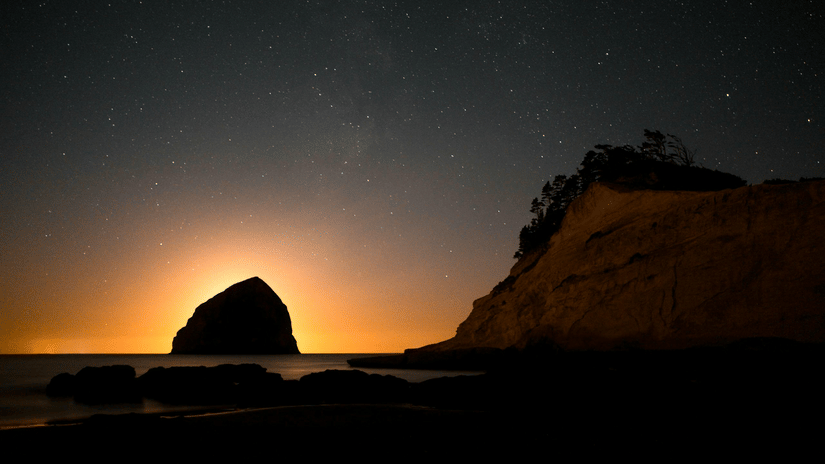 A beautiful silhouette of a huge rock cliff formed due to the sunset, merging with the night sky on a beach.