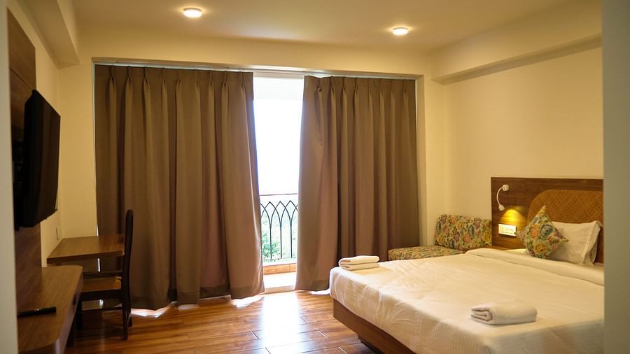 A room with a double bed, a work desk, and a TV hung on the wall in front of the bed. - VITS Kunjham Retreat, Gangtok