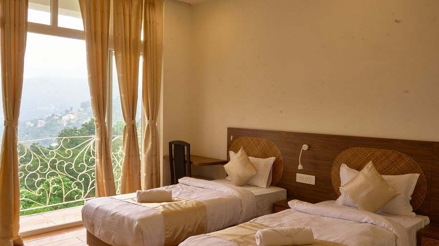 A room with matching twin beds, pillows, and a large window with drapes. - VITS Kunjham Retreat, Gangtok