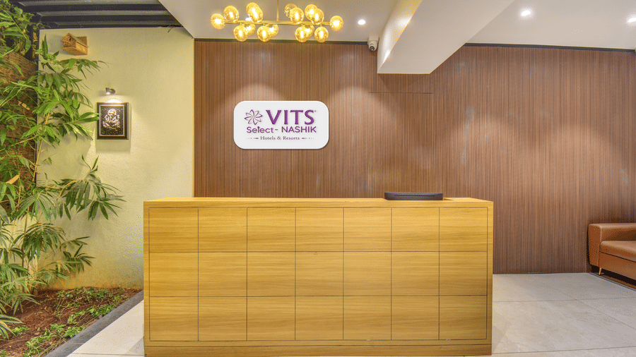 Reception area of VITS Select Nashik Hotels & Resorts featuring the logo of the property on the other side of the reception desk and a plant next to it