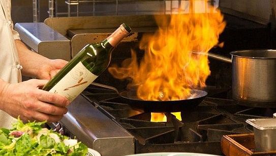 A chef ignites the wok with a splash of alcohol, creating a fiery burst to elevate the dish - Brewery Gulch Inn & Spa