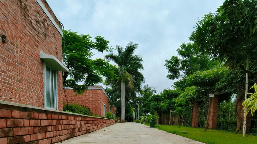 A straight, wide, stone-paved pathway leading up a slight incline between a patch of green grass and a tall red brick building on the left | Nandan Resort