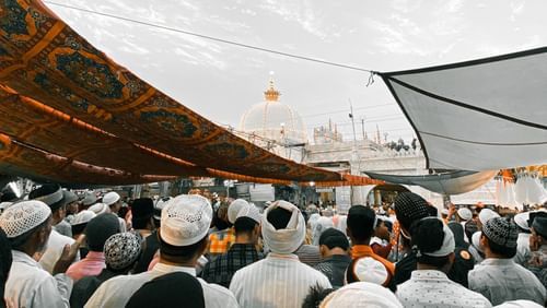 A crowd of people with coverings over their heads, seen from behind, under a cloudy sky.